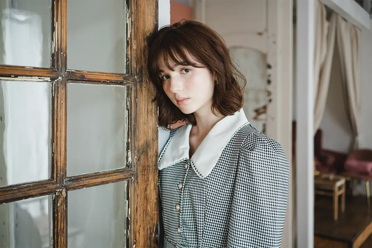 Portrait of a woman indoors leaning against a wooden doorframe photographed with a Tamron fast zoom lens for Nikon Z mount.