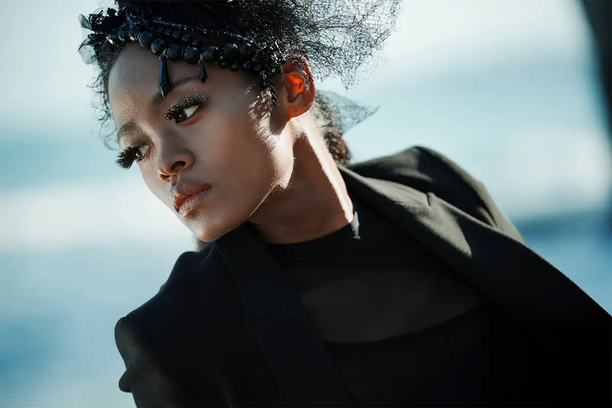 Retrato de una mujer con un atuendo negro y un tocado decorativo, fotografiada al aire libre con un suave desenfoque del fondo.