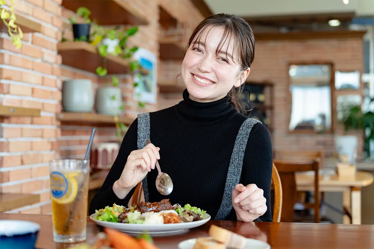 Femme souriant à la table d'un restaurant, capturée avec une compression flatteuse de 85 mm et un flou d'arrière-plan naturel.