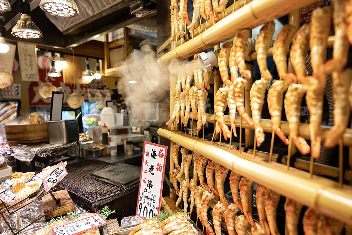 Shrimp skewers steaming at a busy street food market in Japan, photographed with a Sony E-mount travel lens for low-light travel and cultural photography.