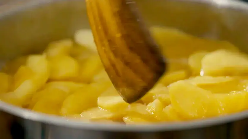 Gros plan d'une spatule remuant des pommes coupées en tranches dans une casserole avec une faible profondeur de champ pour une scène de cuisine cinématographique.