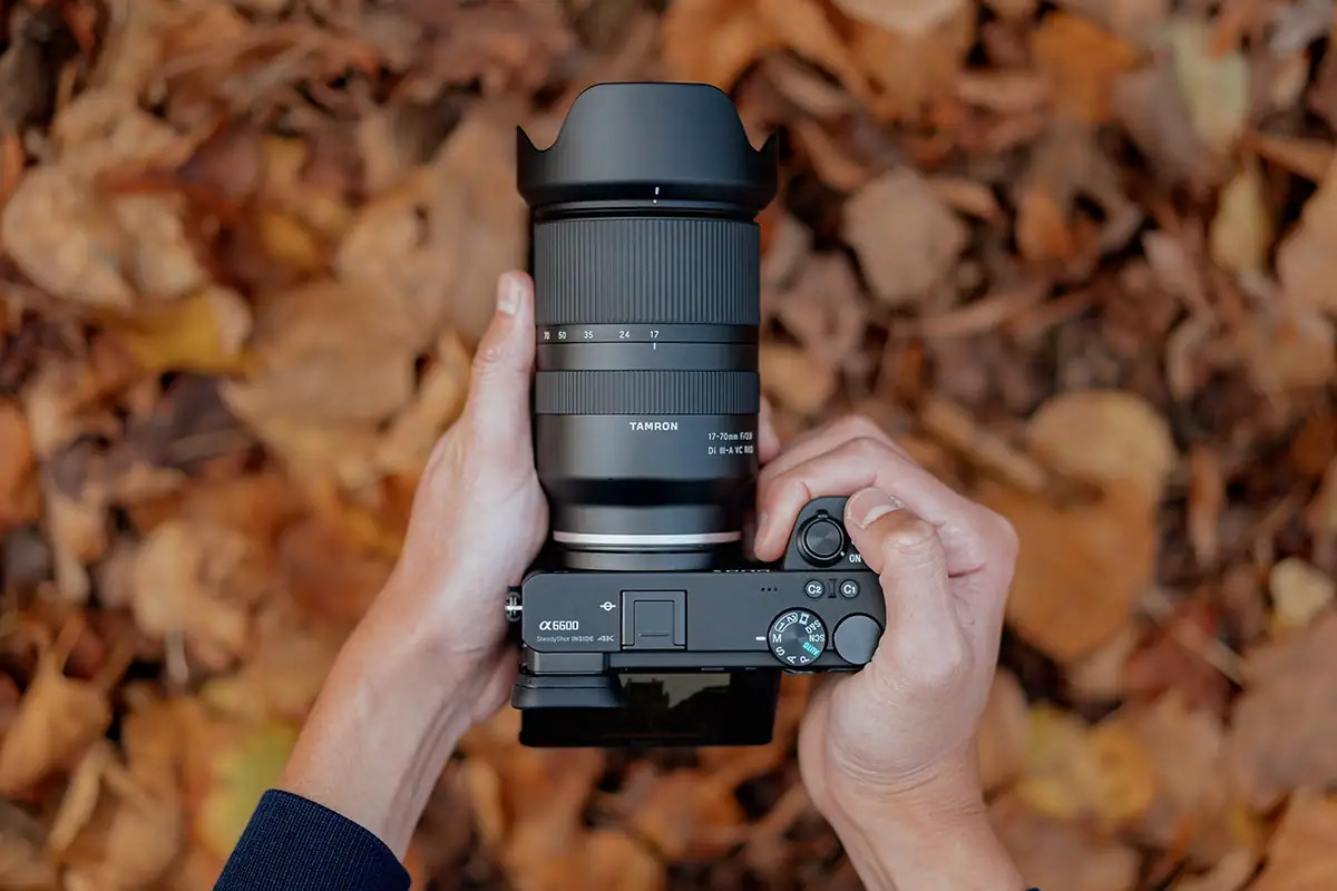 Lente Tamron 17-70 mm F/2.8 Di III-A VC RXD (modelo B070) montado en una cámara sin espejo Sony APS-C sostenida sobre hojas otoñales.