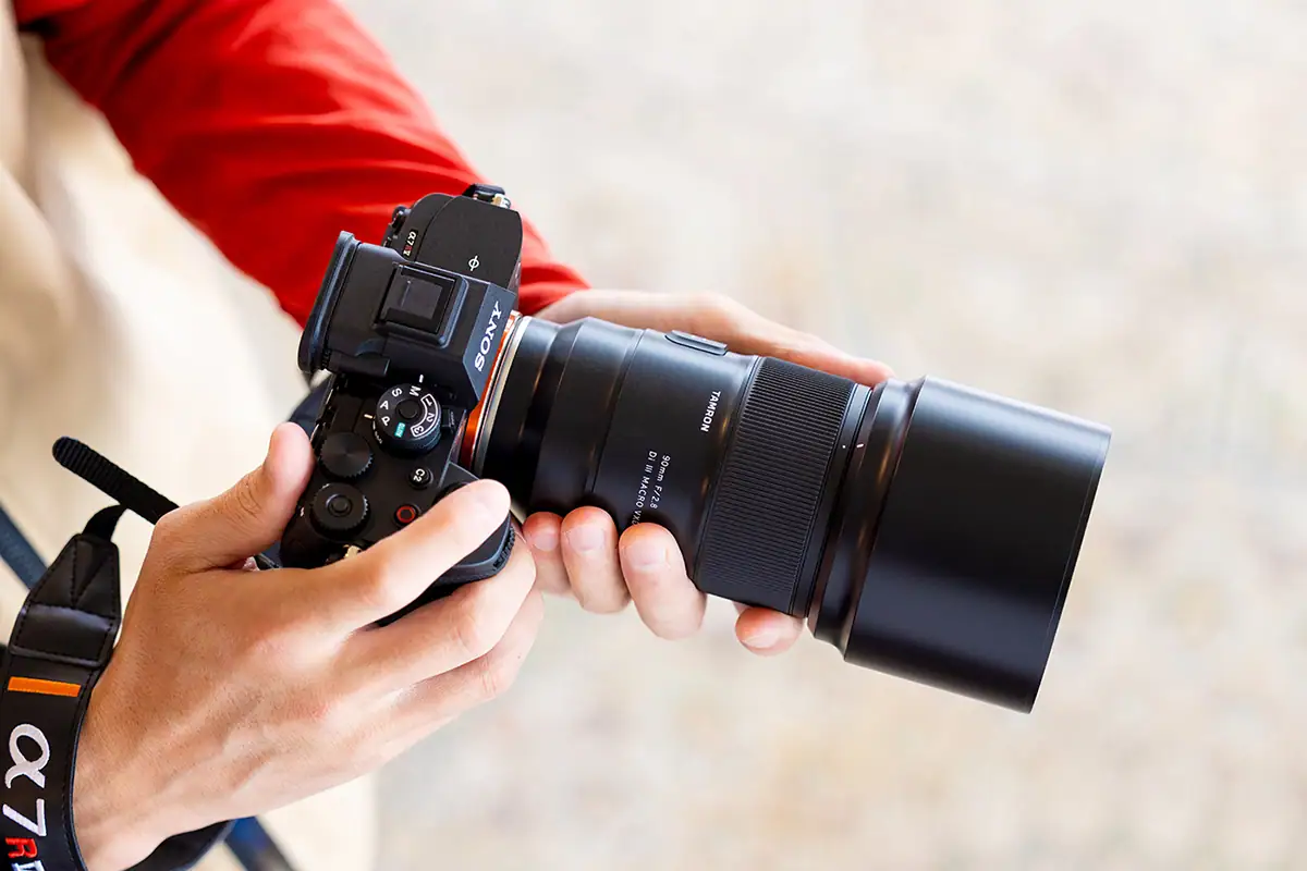 Lente Tamron 90 mm F/2.8 Di III VXD 1:1 Macro (modelo F072) montado en una cámara sin espejo Sony sostenida con la mano.