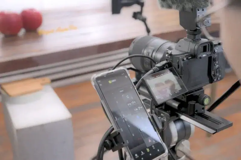 Behind-the-scenes view of a camera rig connected to a smartphone running Tamron Lens Utility Mobile.