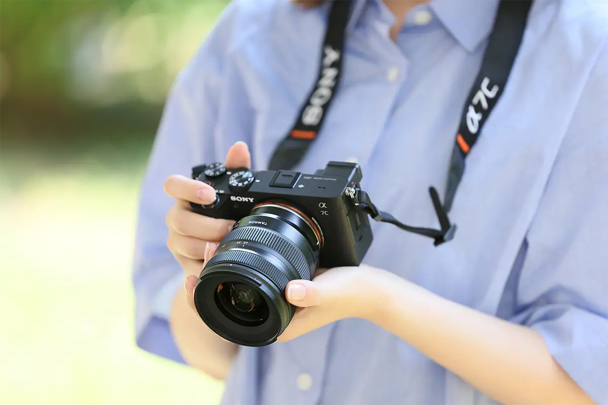 Lente zoom estándar Tamron montado en una cámara sin espejo Sony a7C sostenida por un fotógrafo al aire libre.