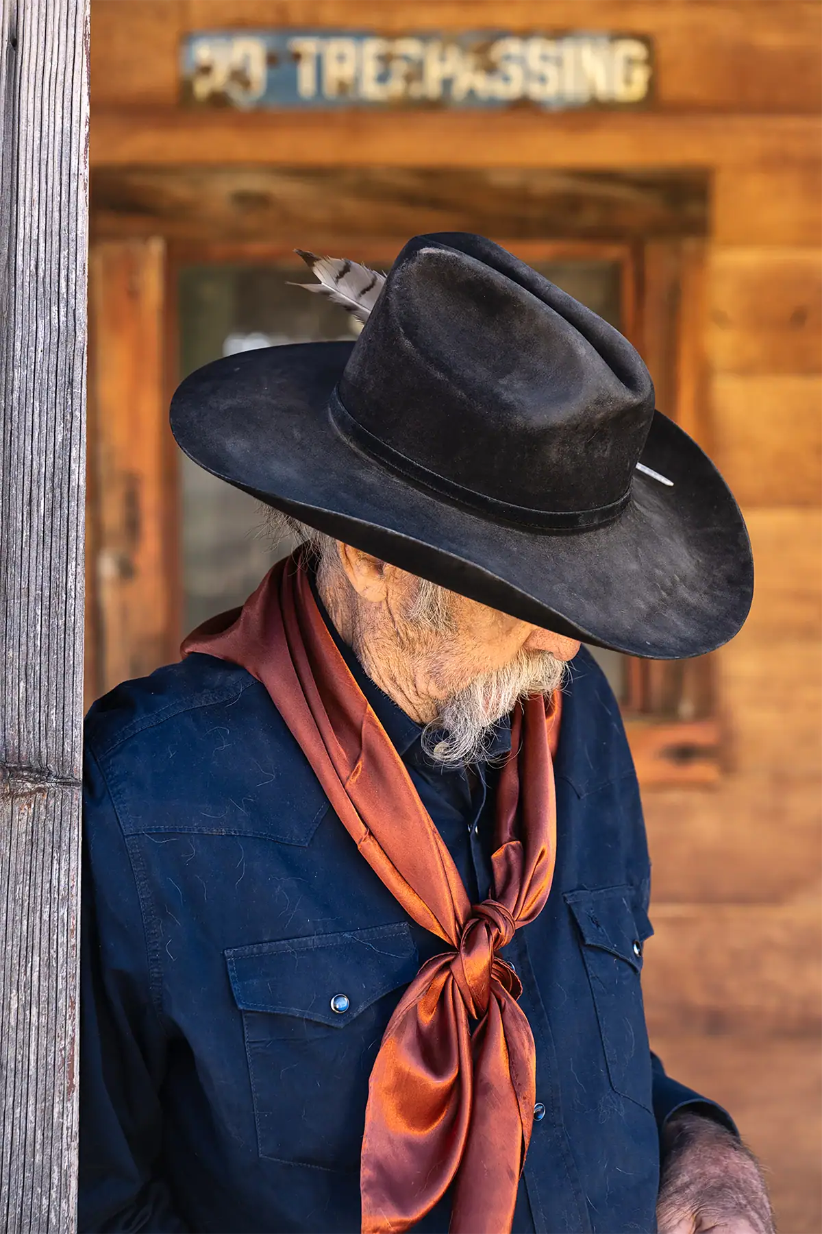 Retrato de caubói olhando para baixo, usando uma bandana vermelha, fotografado com a lente Tamron 35-100 mm F/2.8 Di III VXD.