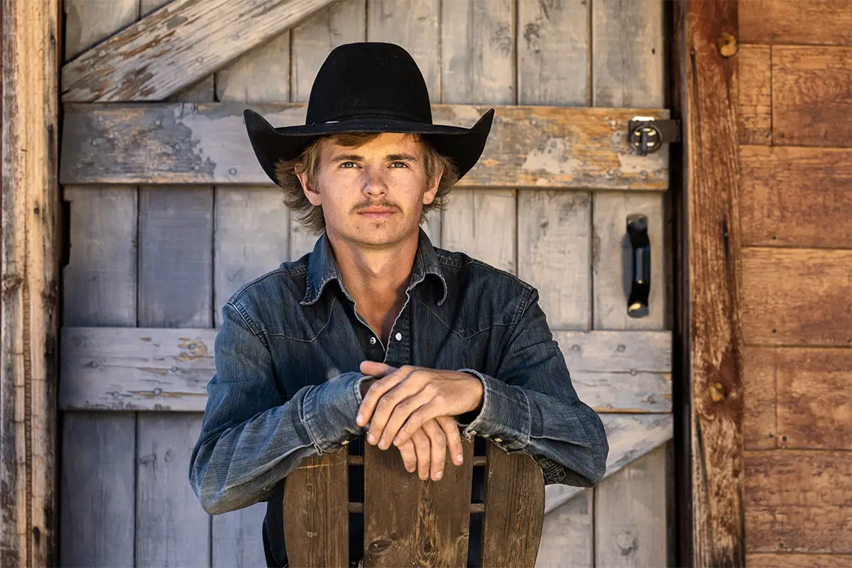 Retrato de um vaqueiro sentado em uma cadeira de madeira fotografado com a lente Tamron 35-100 mm F/2.8 Di III VXD.