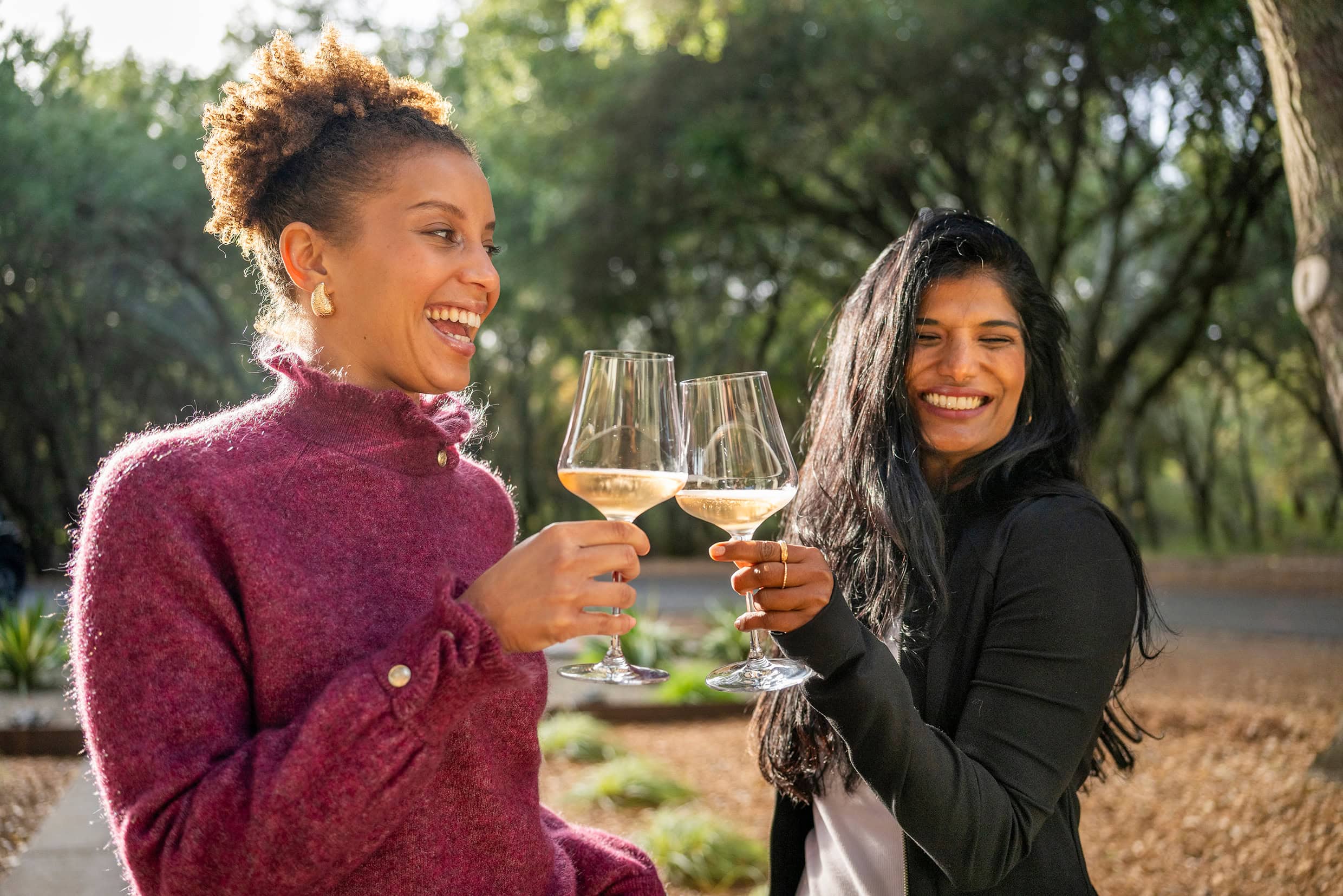 Dos mujeres riendo al aire libre mientras sostienen unas copas, en un retrato espontáneo.
