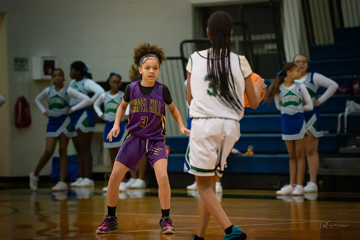 Two girls playing basketball and one is defending the other on the court