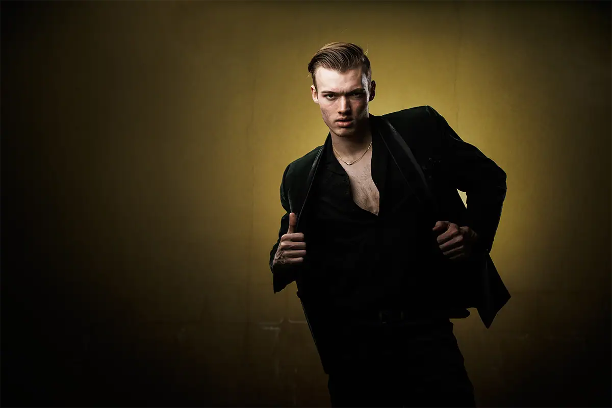 Man in a black suit lit with directional moody portrait lighting that creates facial shadow and strong contrast.