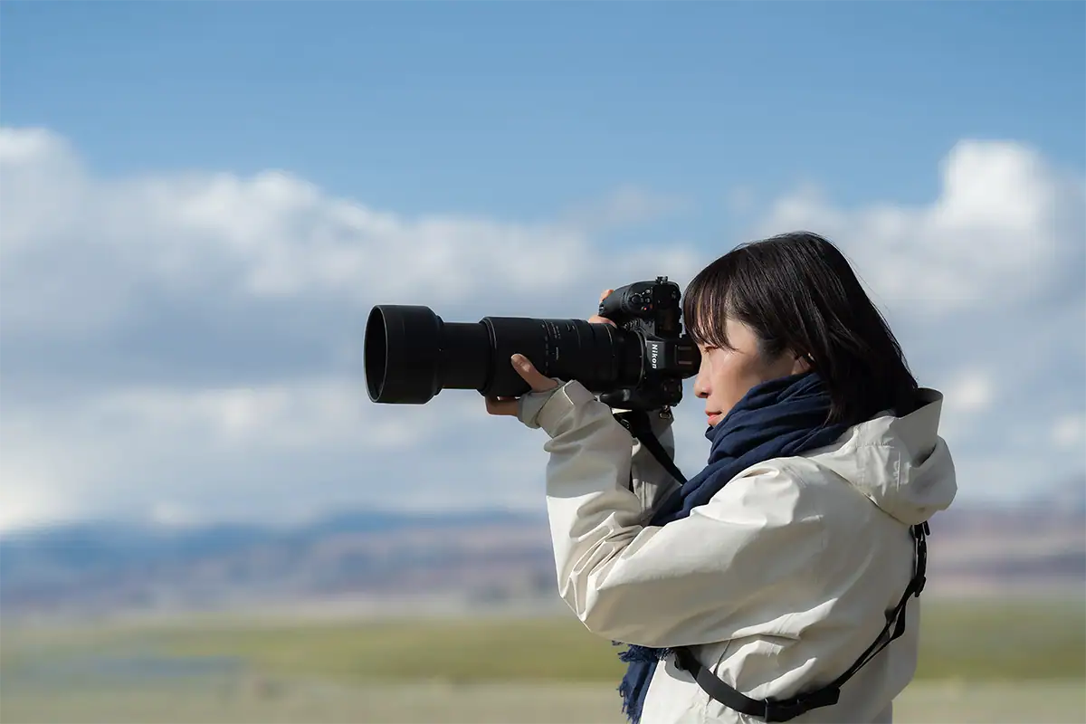 Photographer using a telephoto lens to capture wildlife outdoors with a clear sky background.