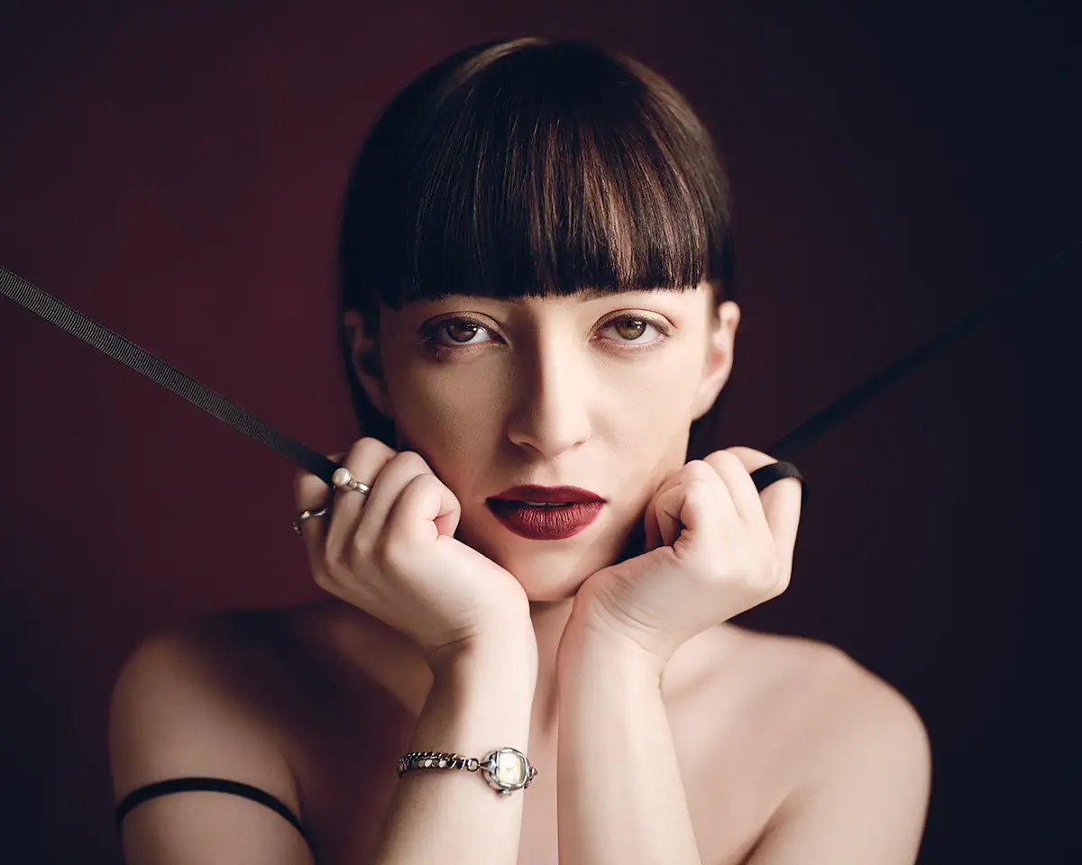 Portrait éditorial en gros plan d'une femme à la frange émoussée, éclairé par une lumière dure contrôlée et des ombres nettes.