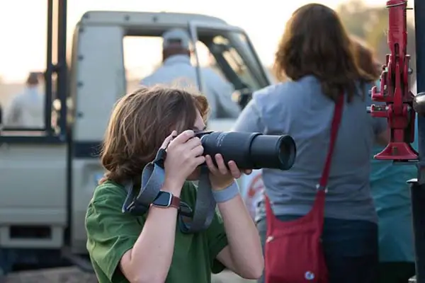 Young photographer using Tamron telephoto lens from safari vehicle to capture wildlife.