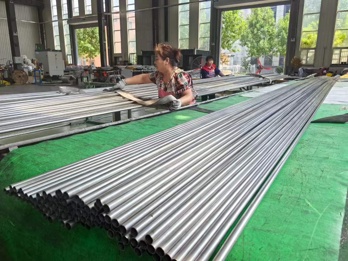 Female factory worker sorting and inspecting polished stainless steel round tubes on production line in Chinese factory