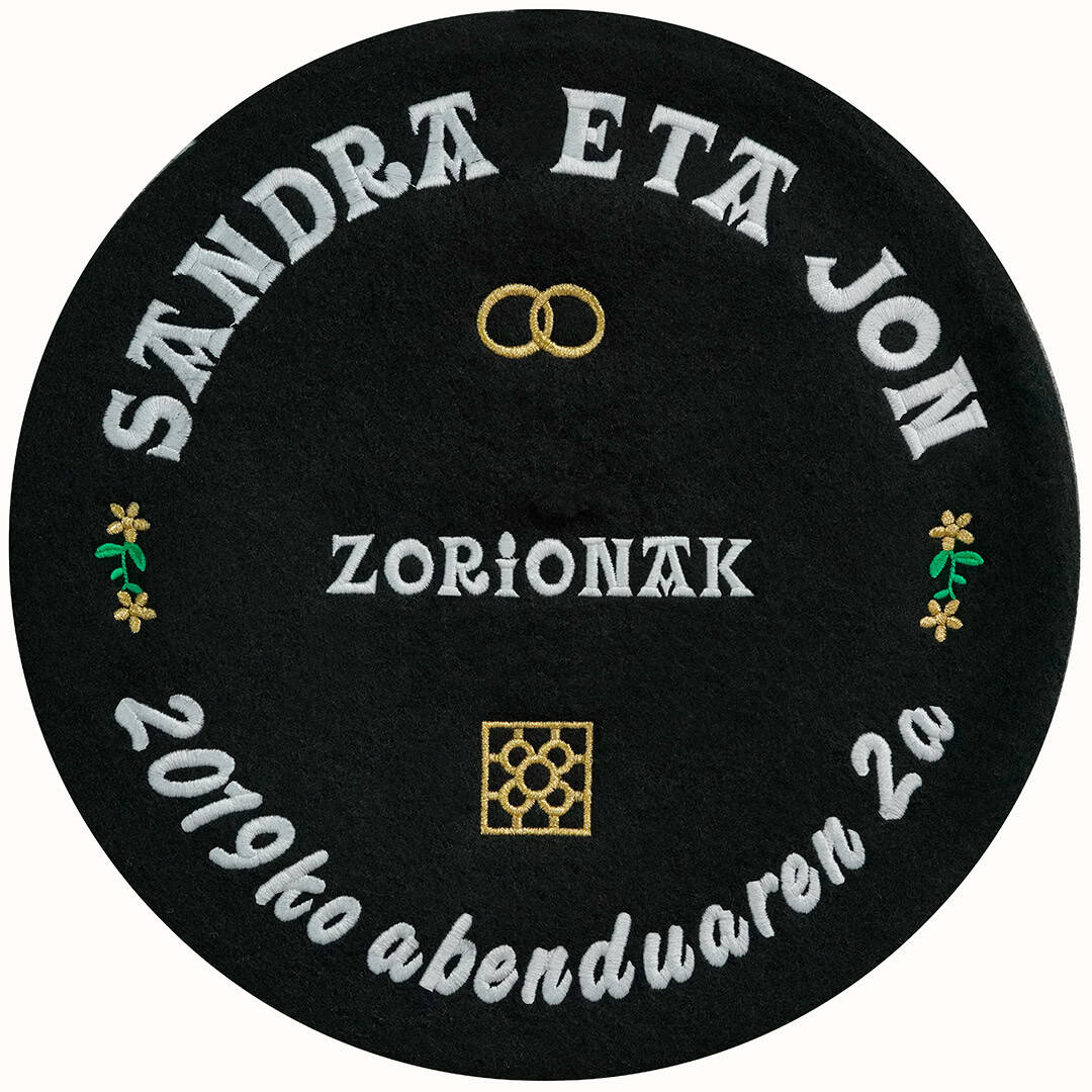 Txapela personalizada para boda bordada con hilos de color oro y blanco con nombres, alianzas, flores y la baldosa de Bilbao