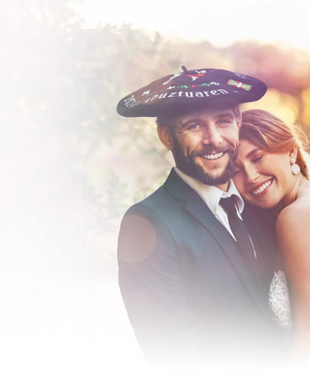 Pareja de novios abrazados luciendo una txapela bordada personalizada en la cabeza del novio