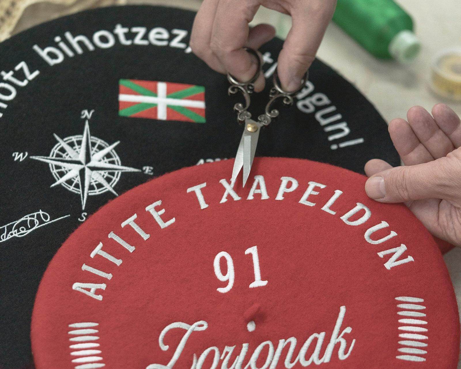 Txapela bordada roja de 13 pulgadas junto a una txapela txapeldun grande negra, ejemplo de medidas según el uso de la pieza en Teletxapela.