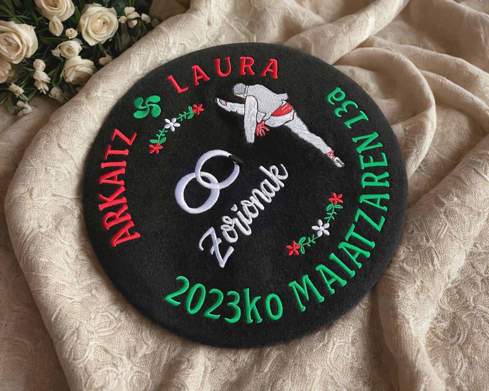 Txapela personalizada para la boda de Arkaitz y Laura, bordada con un aurreskulari, alianzas, lauburu y lazos de flores sobre paño negro