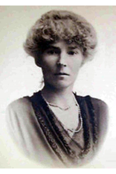 Black and white portrait of Gertrude Bell with curly hair and elegant attire.