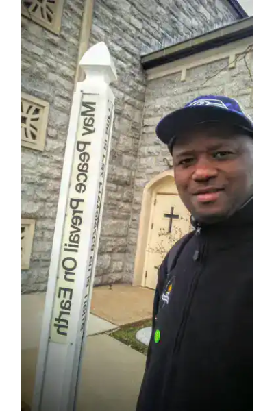 Man standing next to The Peace Pole at a churchyard.