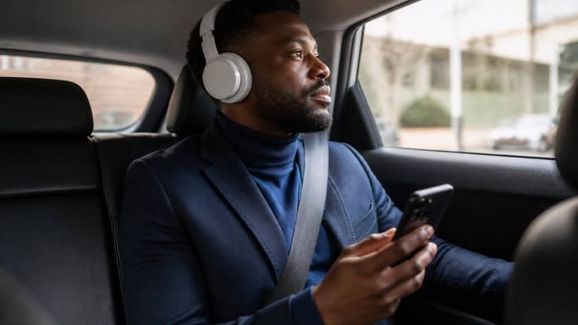 Man listening to audiobooks in car with headphones and smartphone.