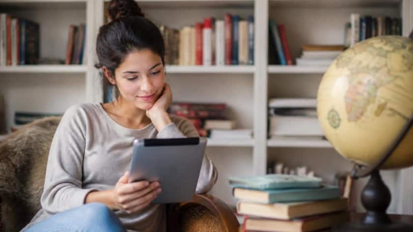Young woman enjoying reading an eBook in a cozy home library.