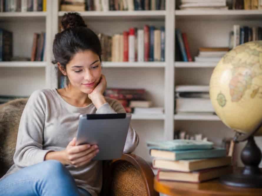 Young woman enjoying reading an eBook in a cozy home library.