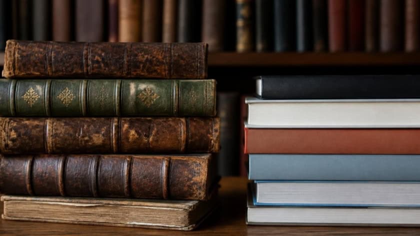 Stack of vintage and modern books on a wooden shelf.