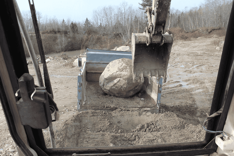 Excavator loading a massive rock into a bucket at a construction site.