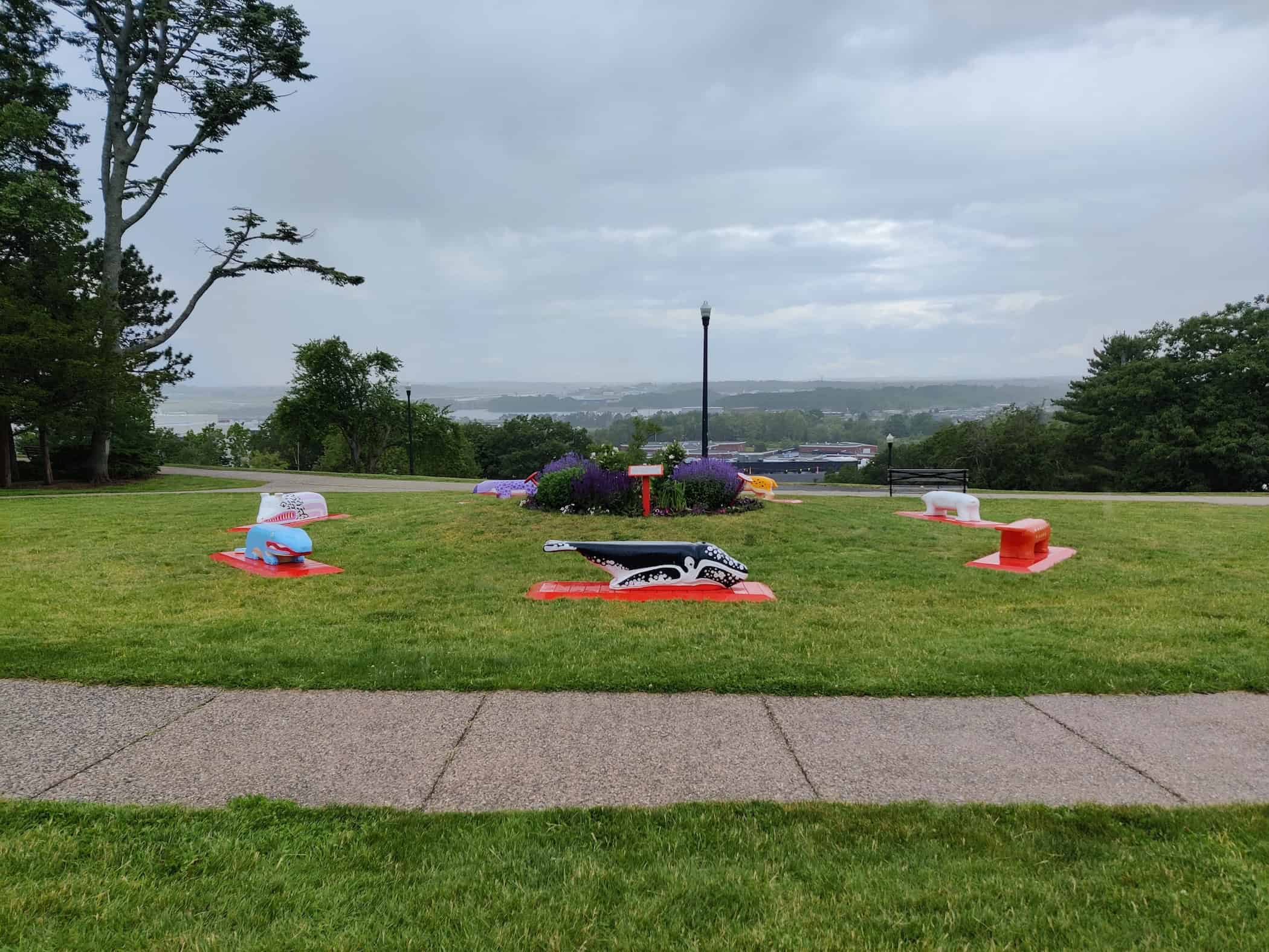 Colorful outdoor sculptures on a grassy hill with scenic view and cloudy sky.
