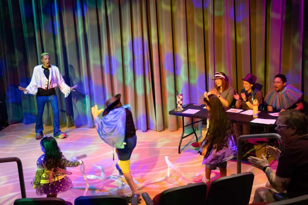 Theater performance with children dancing and adults watching on stage.