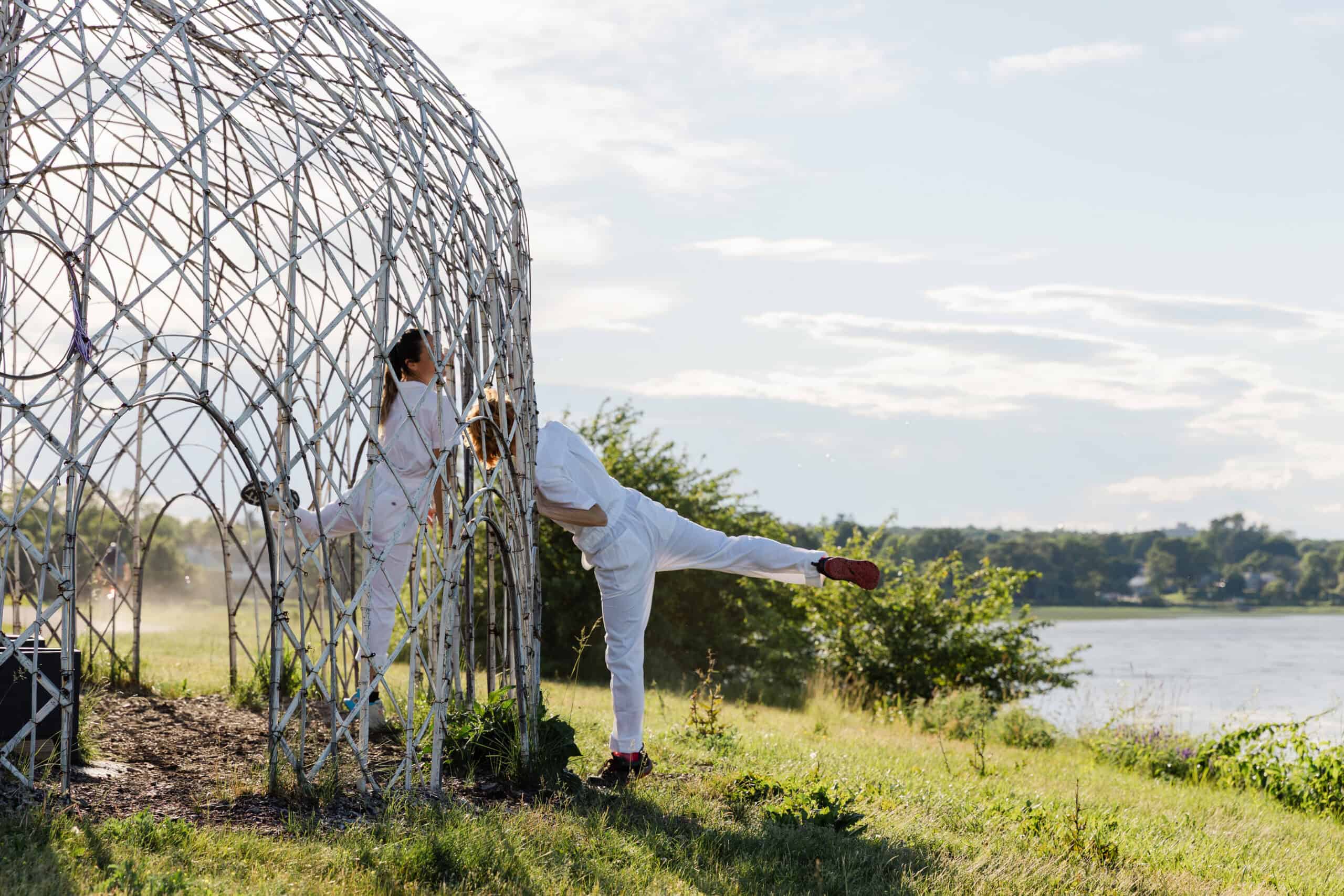 People interacting with a modern outdoor art sculpture near a lake.