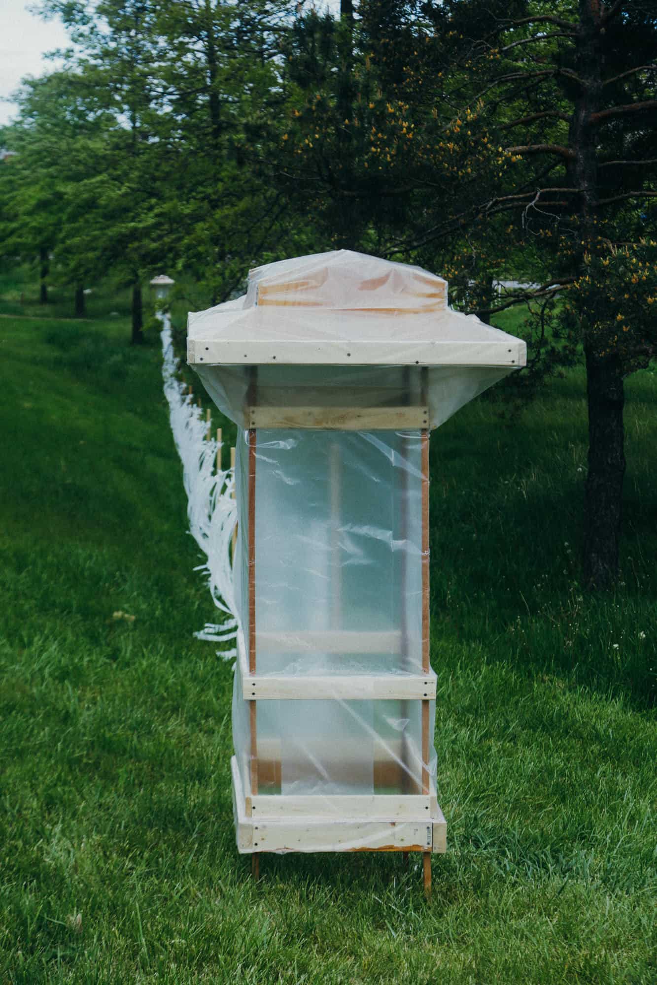 Portable greenhouse structure with plastic cover in a lush green park.