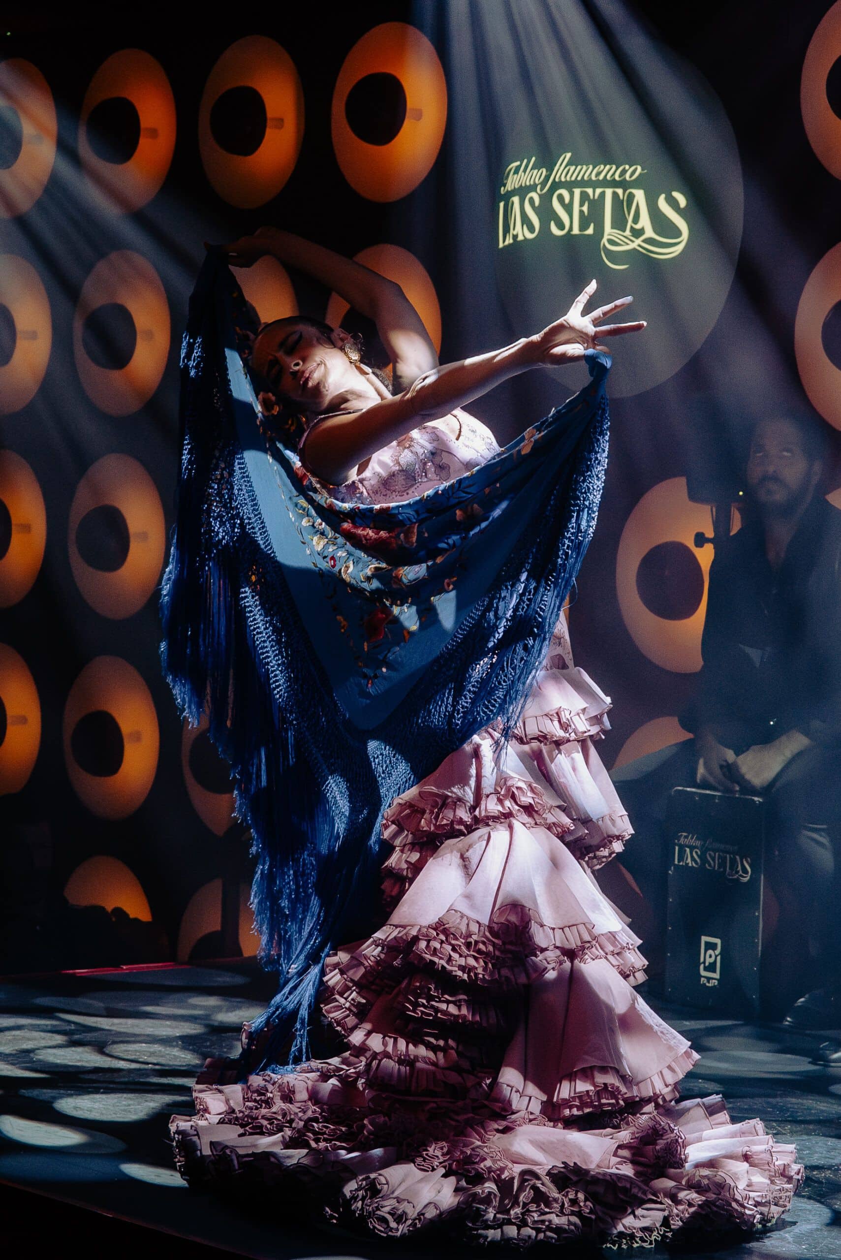 Bailaora flamenca profesional con mantón azul y vestido rosa interpretando baile flamenco en el escenario del Tablao Las Setas de Sevilla