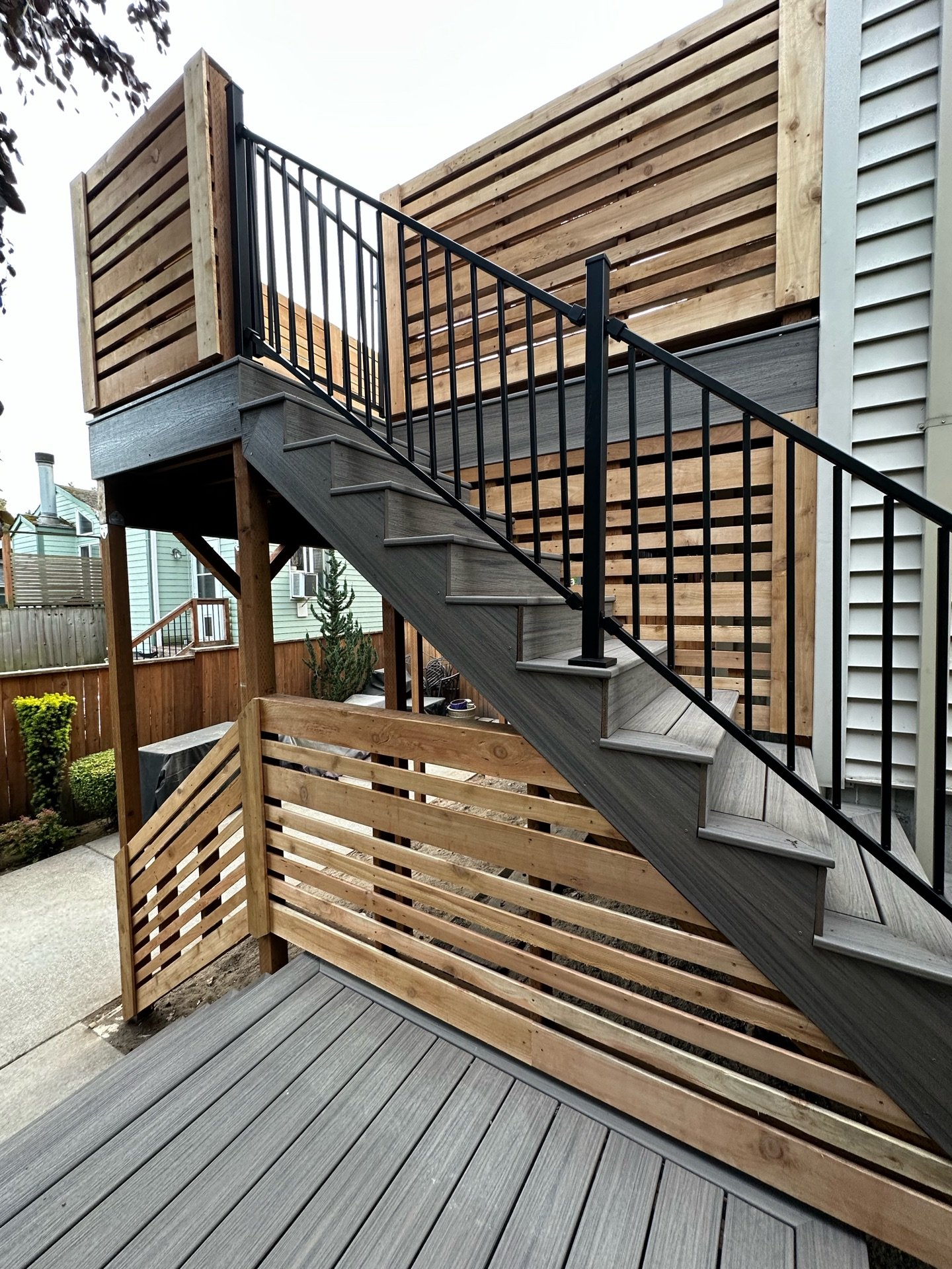 Outdoor deck stairs with wooden fencing and metal railing.