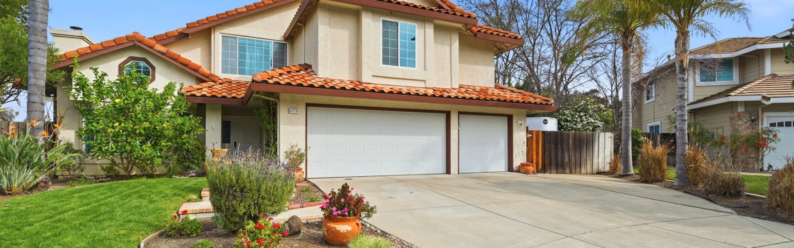 Elegant Walnut Creek residence featuring lush green lawn, colorful plants, and a spacious driveway.