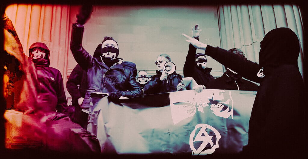 Order Of Nine Angles (O9A): The Nazi-Occult Network Built For Radicalization Masked Protesters Holding Signs During An Underground Demonstration.