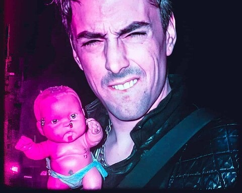 Eerie image of a man holding a disturbing doll with neon lighting.