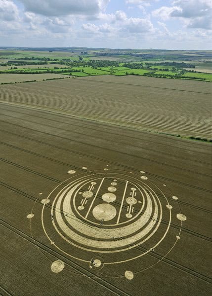 Crop circle design in a vast agricultural field under a partly cloudy sky.