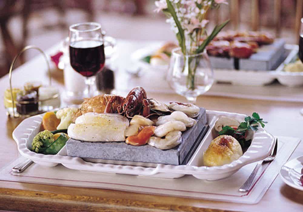 Fresh seafood platter at The Flames Galore restaurant, featuring oysters, lobster, and shrimp with wine on a stylish dining table.