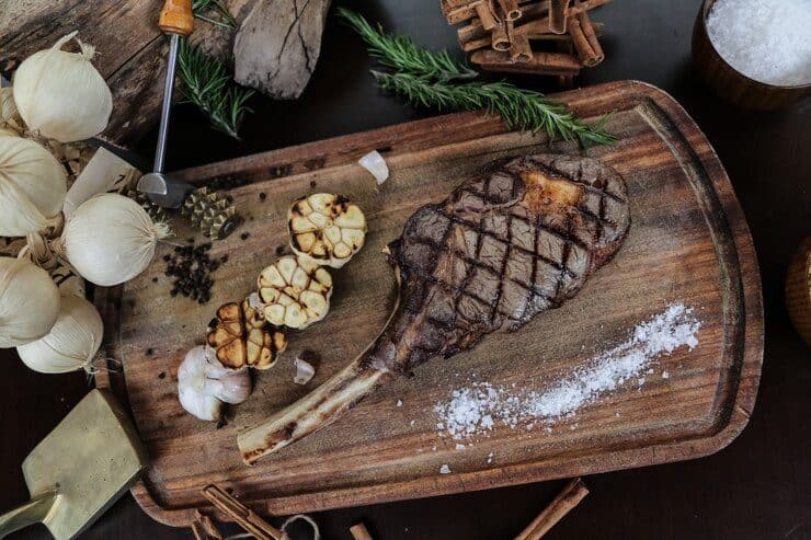 Juicy grilled tomahawk steak with garlic and herbs on rustic wooden board.