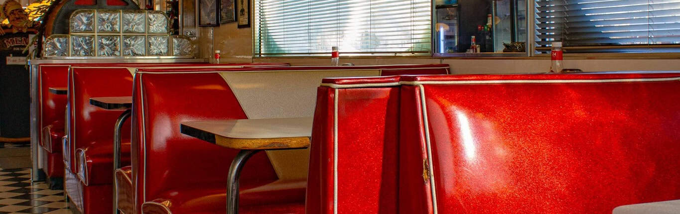 Vintage American diner booth seating with red upholstery and checkered black-and-white floor.