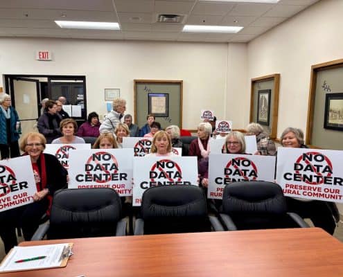 Protesters holding signs against the data center development in Fostoria, emphasizing preserving rural community identity.