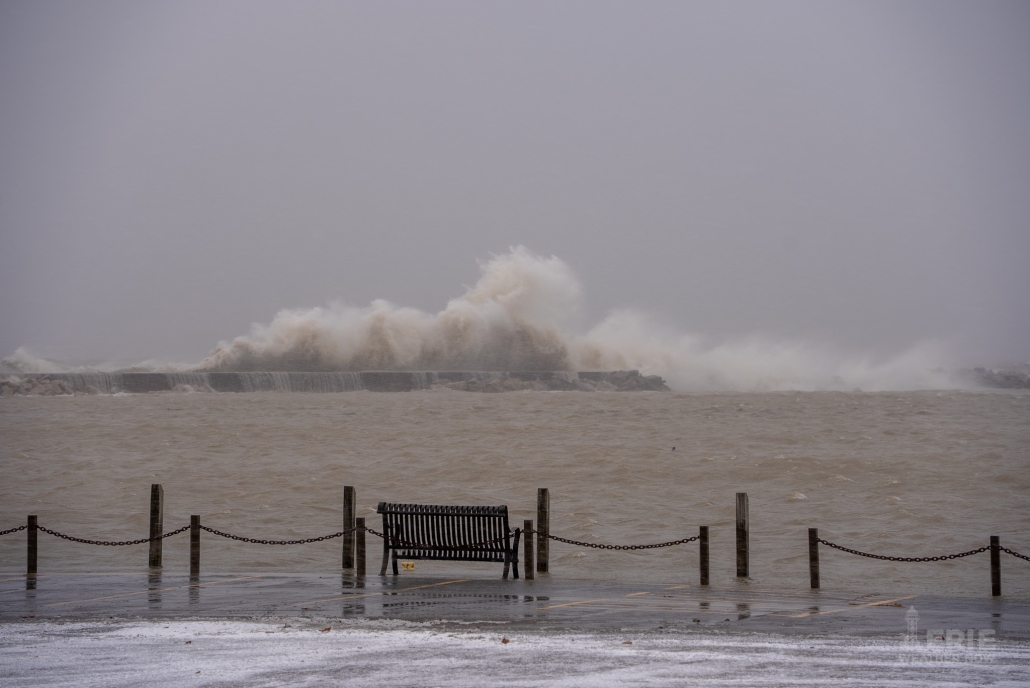 High waves crashing on a rocky pier during stormy weather, causing large splashes and turbulent sea conditions.
