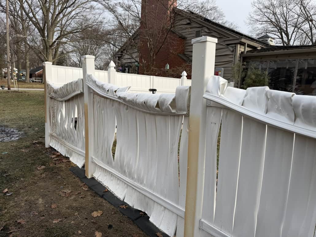 A damaged white fence in Fostoria with torn sections, wet from recent rain, in a residential yard.