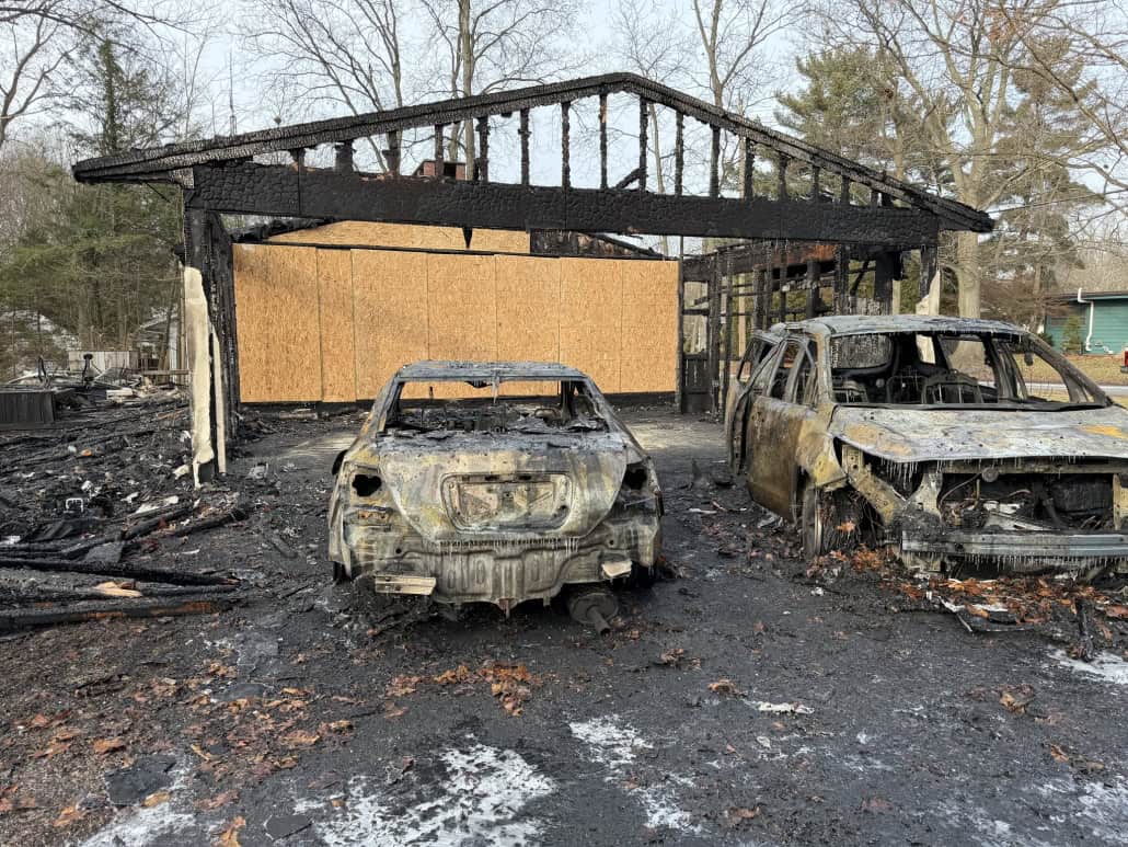 Charred, destroyed vehicles and smoke-damaged structure after fire incident.