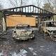 Charred and destroyed cars in front of a burned-down house following an intense fire.
