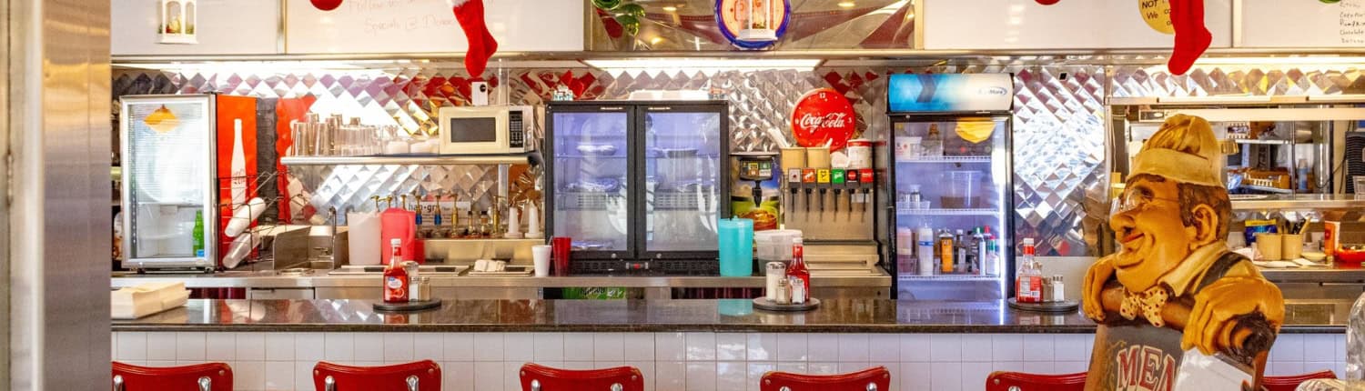 A cozy retro diner decorated for Christmas with red chairs, stocking garlands, and a smiling chef statue.