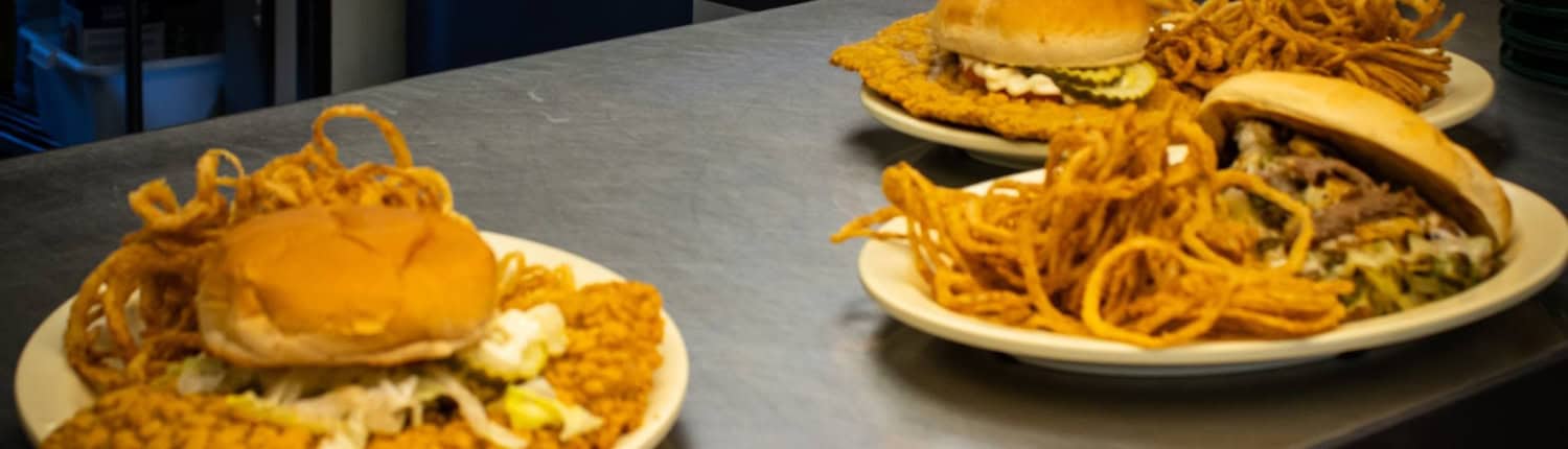 Delicious fried chicken sandwiches with crispy onion rings on white plates, served at a diner.