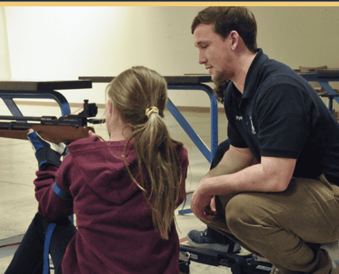 Young girl practicing rifle shooting with instructor.